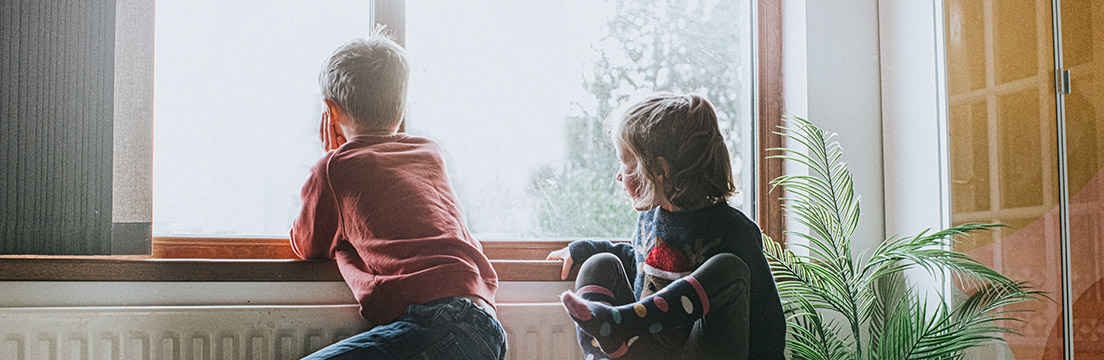 Zwei Kinder sitzen am Fenster und blicken nach draussen – gemütlicher Moment im neuen Zuhause
